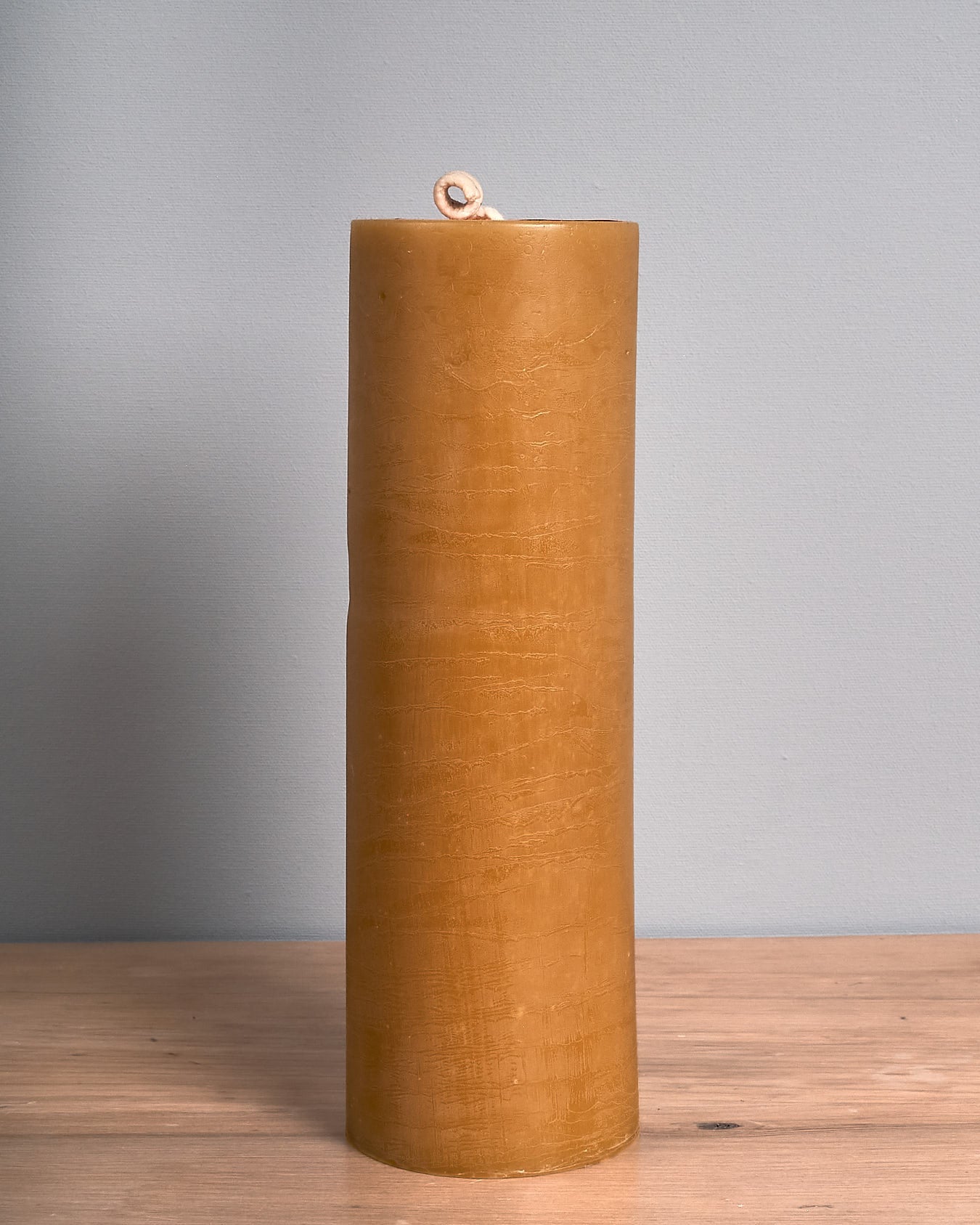 The Pillar Beeswax Candle – Extra Large by Hohepa Candles, with its tall and cylindrical shape, is displayed on a wooden surface against a plain gray background, highlighting its warm beige hue.