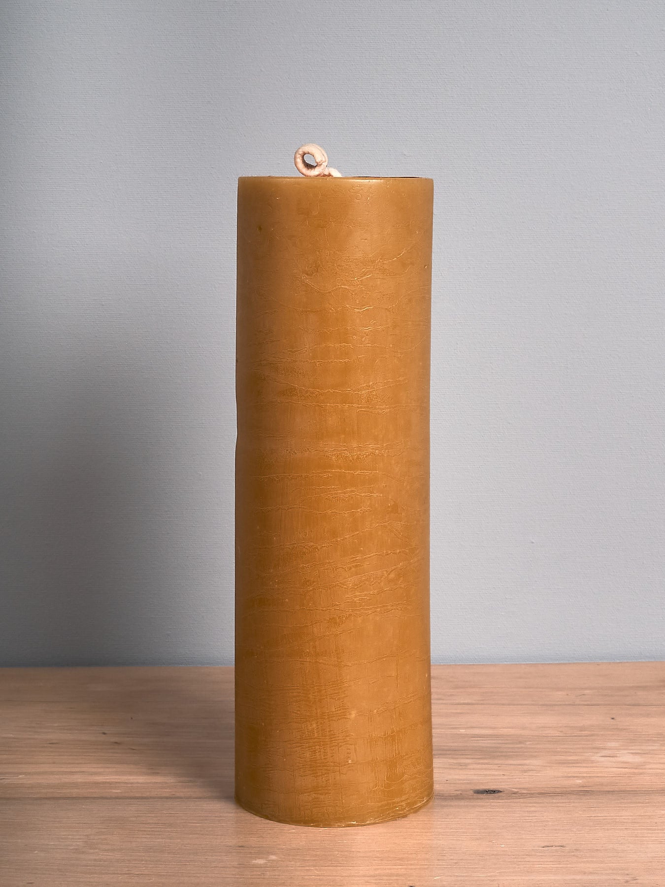 The Pillar Beeswax Candle – Extra Large by Hohepa Candles, with its tall and cylindrical shape, is displayed on a wooden surface against a plain gray background, highlighting its warm beige hue.