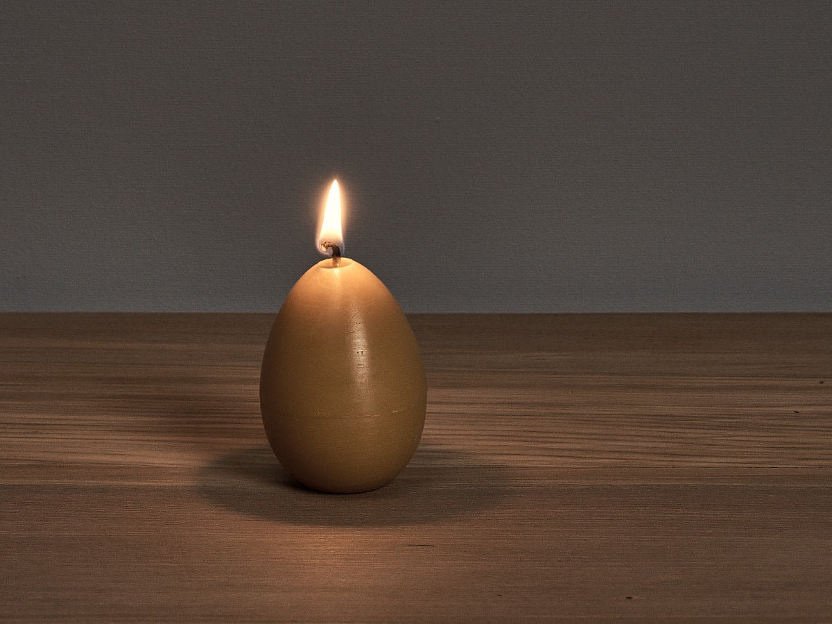 An Egg Candle sitting on a wooden table by Hohepa Candles.
