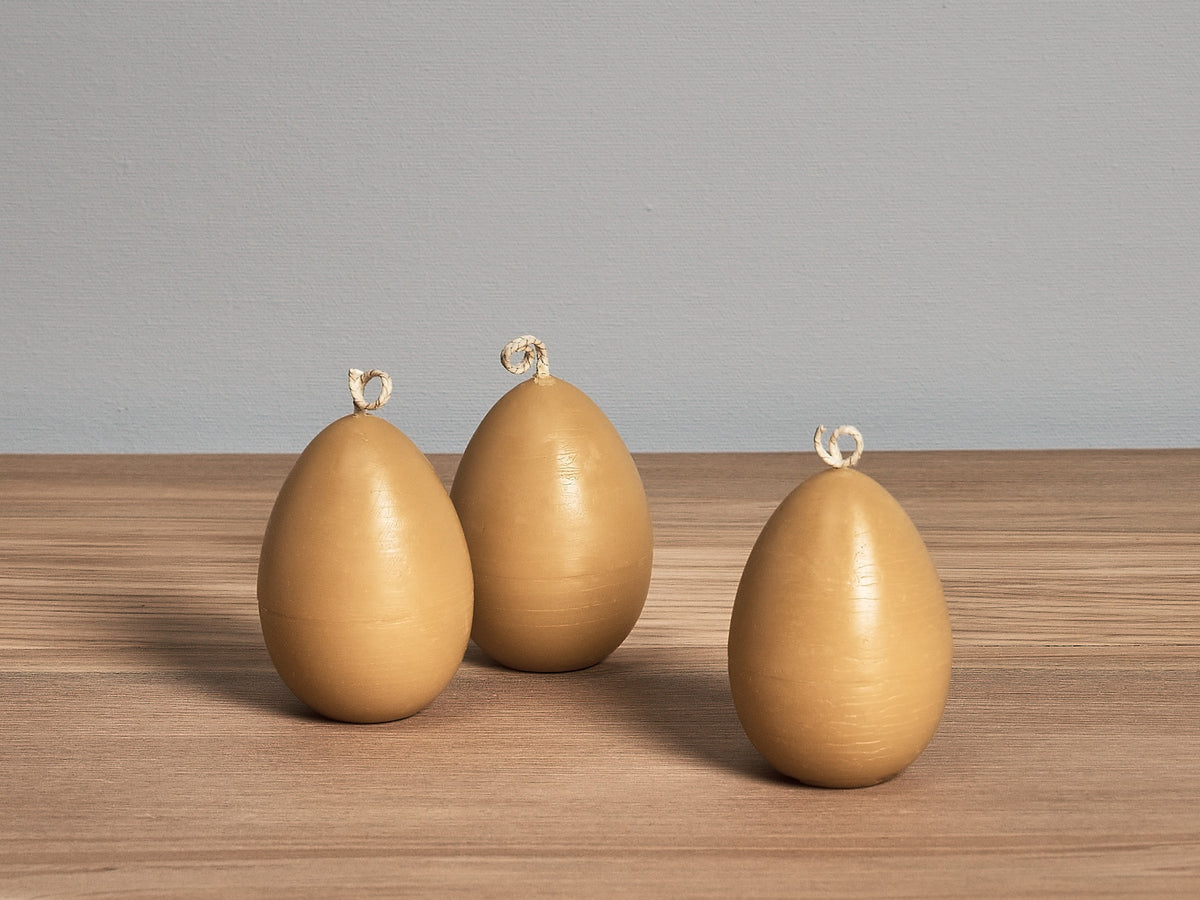 Three Hohepa Candles Egg Candles sitting on top of a wooden table.