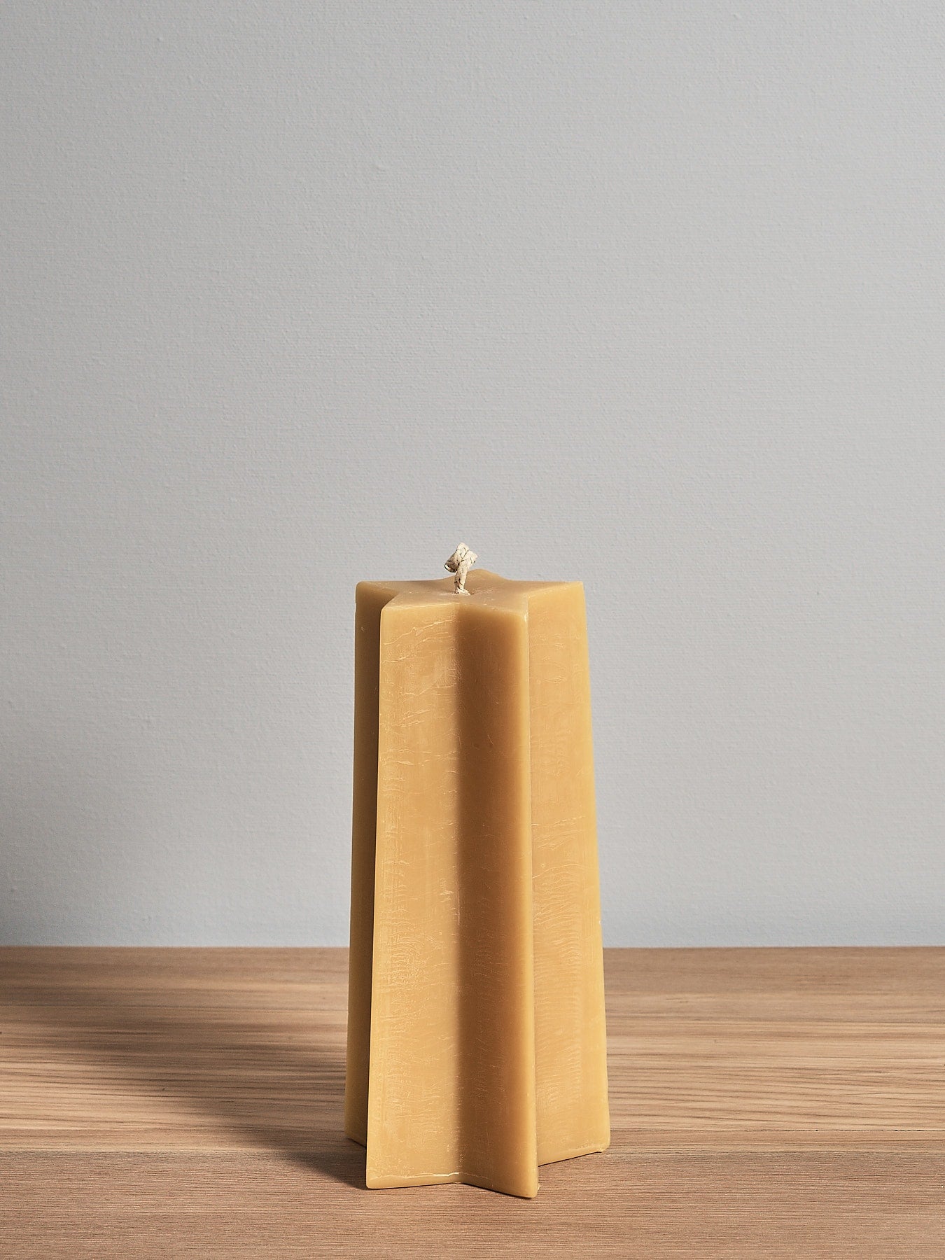 The Star Pillar Beeswax Candle by Hohepa Candles, crafted with natural beeswax, is elegantly displayed on a wooden surface against a light gray background, showcasing the artisanal charm of New Zealand craftsmanship.