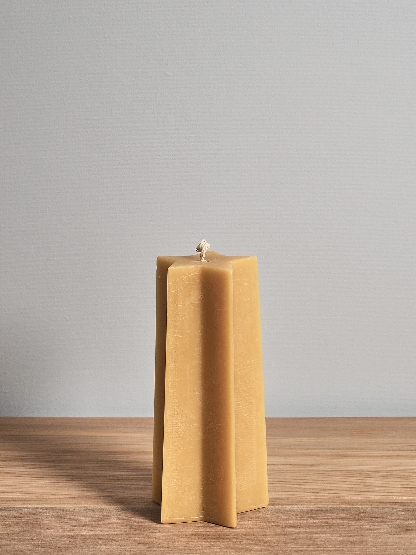 A Star Pillar Candle by Hohepa Candles sitting on top of a wooden table.