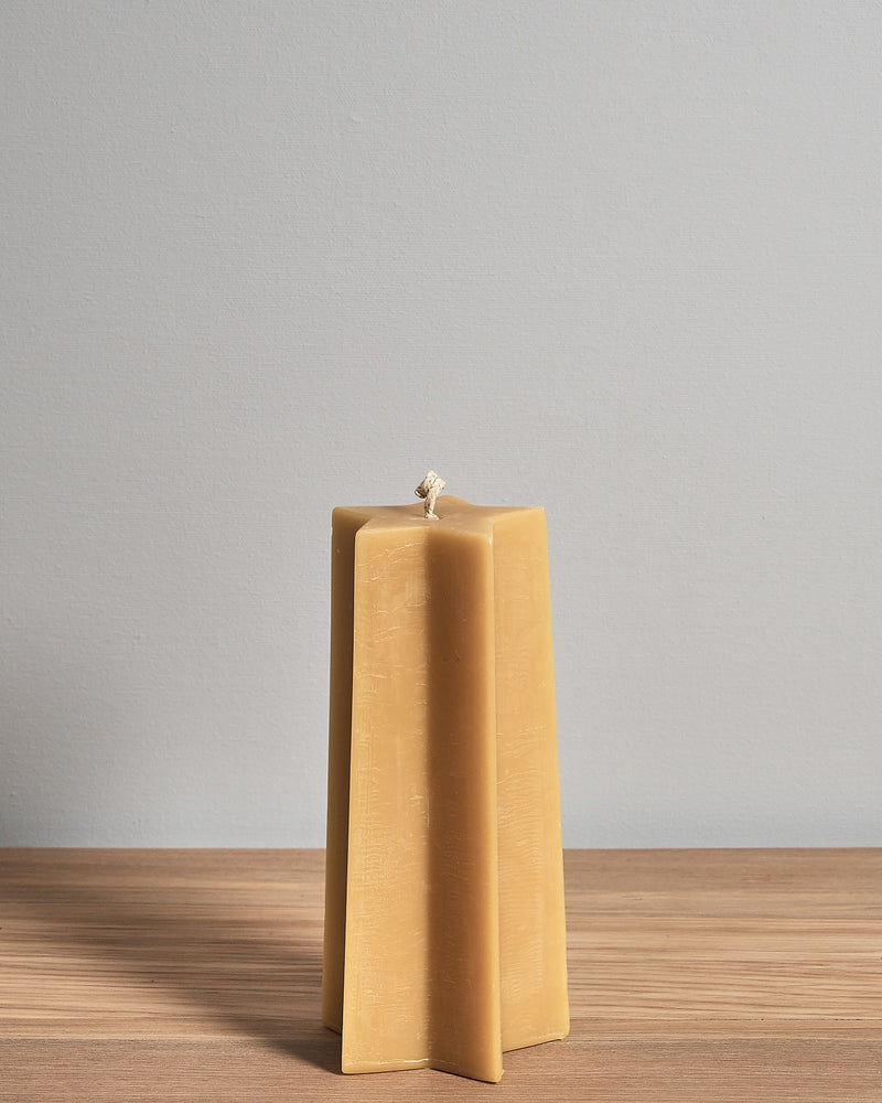 The Star Pillar Beeswax Candle by Hohepa Candles, crafted with natural beeswax, is elegantly displayed on a wooden surface against a light gray background, showcasing the artisanal charm of New Zealand craftsmanship.
