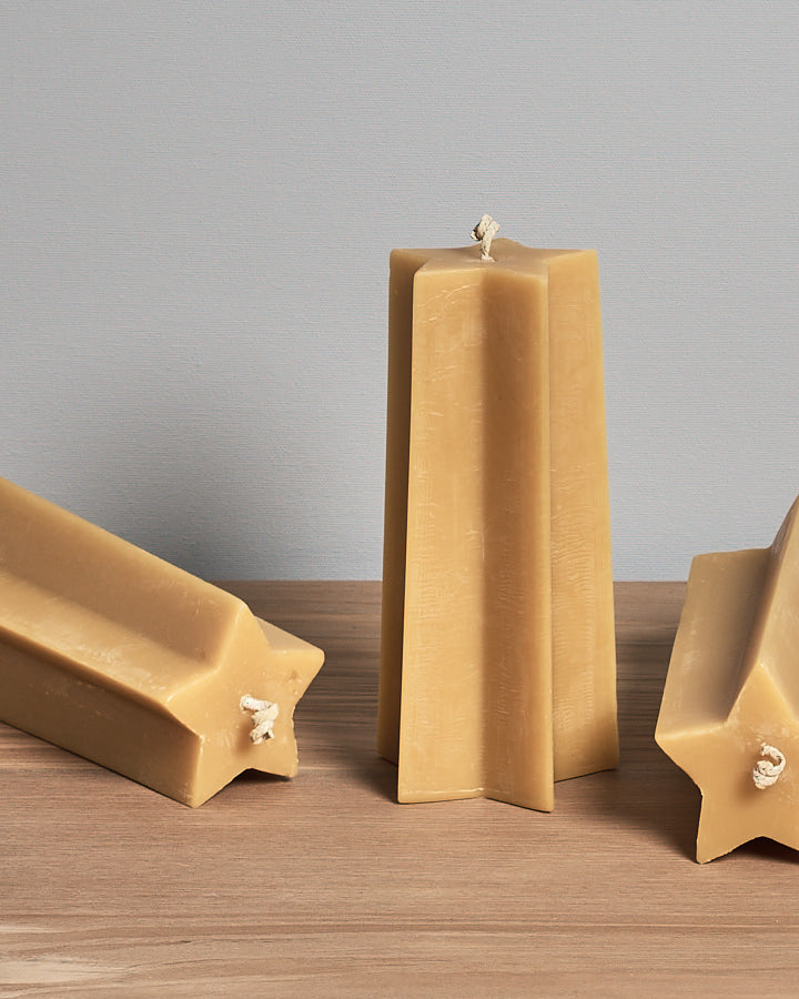 The Star Pillar Beeswax Candle by Hohepa Candles, crafted with natural beeswax, is elegantly displayed on a wooden surface against a light gray background, showcasing the artisanal charm of New Zealand craftsmanship.