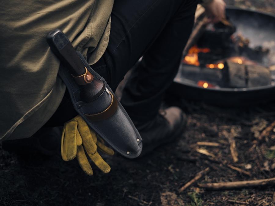 A person holding a Hori Hori Garden Knife &amp; Sheath by Barebones next to a fire.