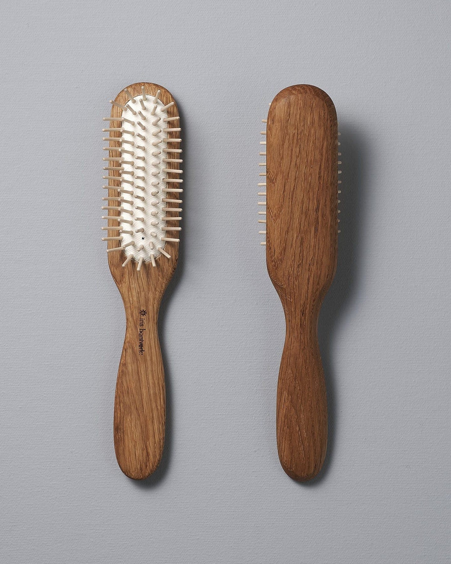 Two Iris Hantverk Oak Hairbrushes with smooth handles, one showing the bristles side with natural rubber pins and the other the back, positioned side by side on a gray background. Perfect for a soothing scalp massage.