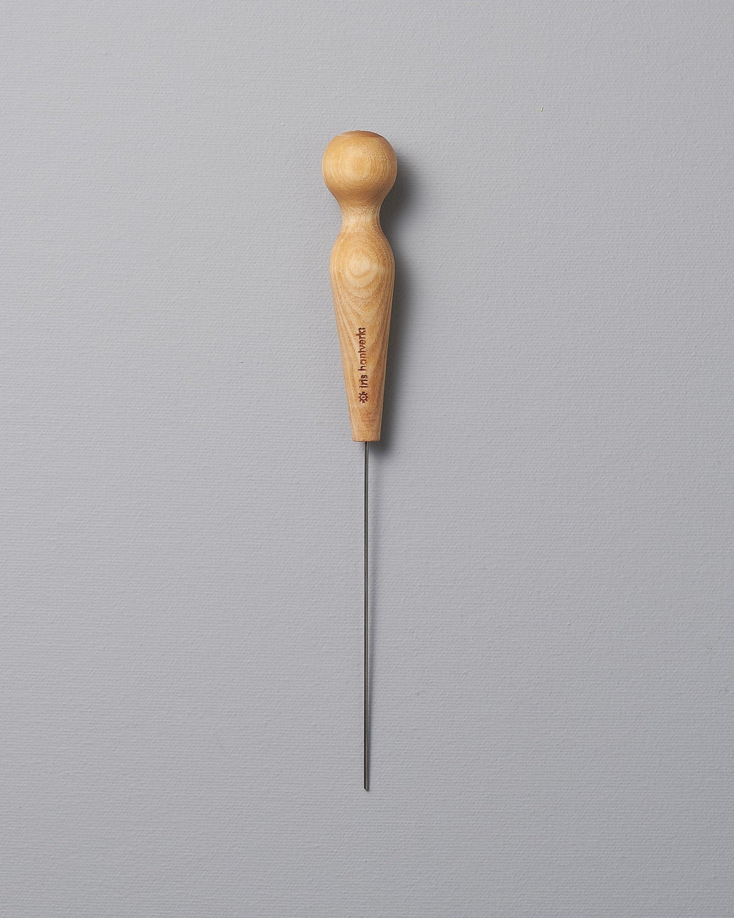 An Iris Hantverk Cake Tester with a wooden handle on a gray background.