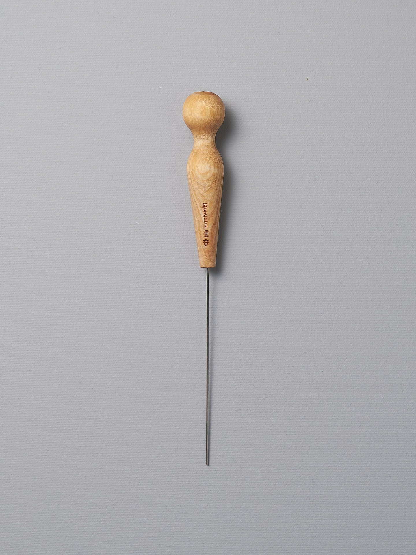 An Iris Hantverk Cake Tester with a wooden handle on a gray background.