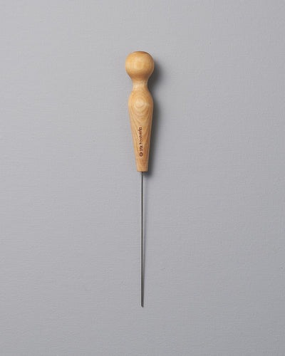 An Iris Hantverk Cake Tester with a wooden handle on a gray background.