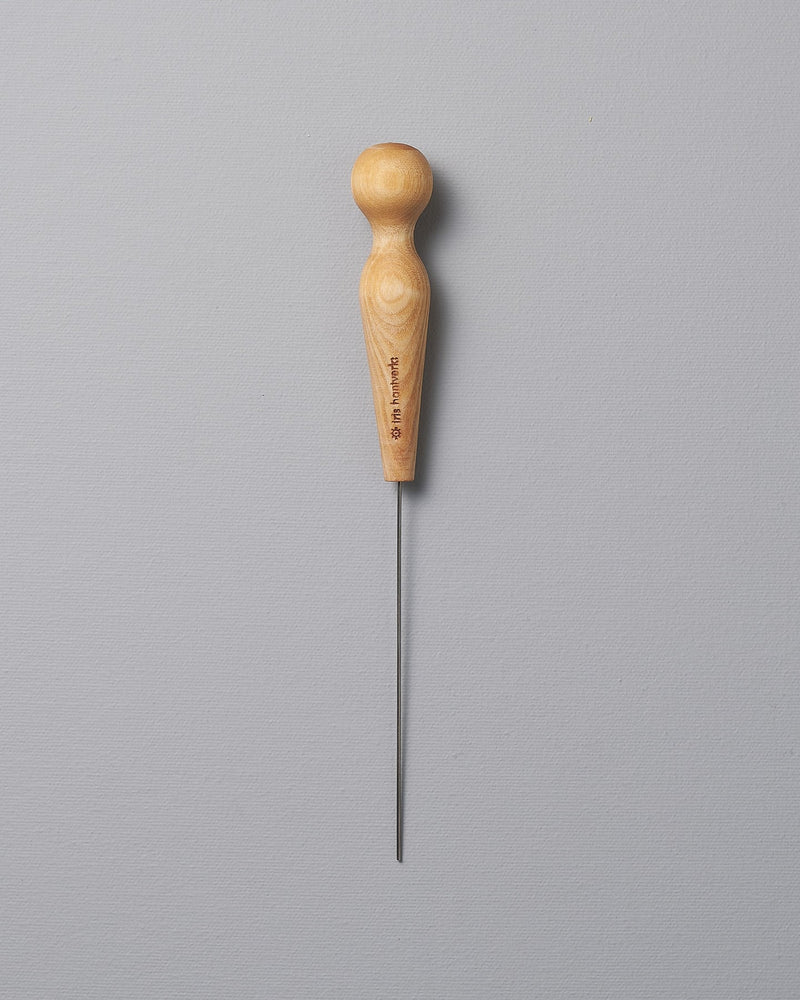 An Iris Hantverk Cake Tester with a wooden handle on a gray background.