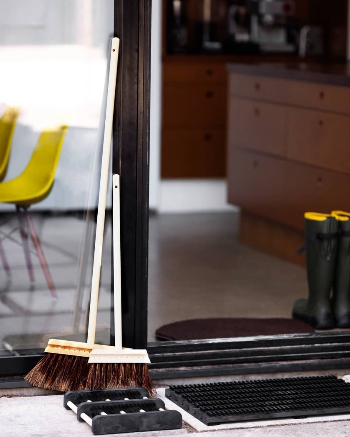 An Outdoor Broom – Birch & Bassine from Iris Hantverk and a broom stand next to a door.