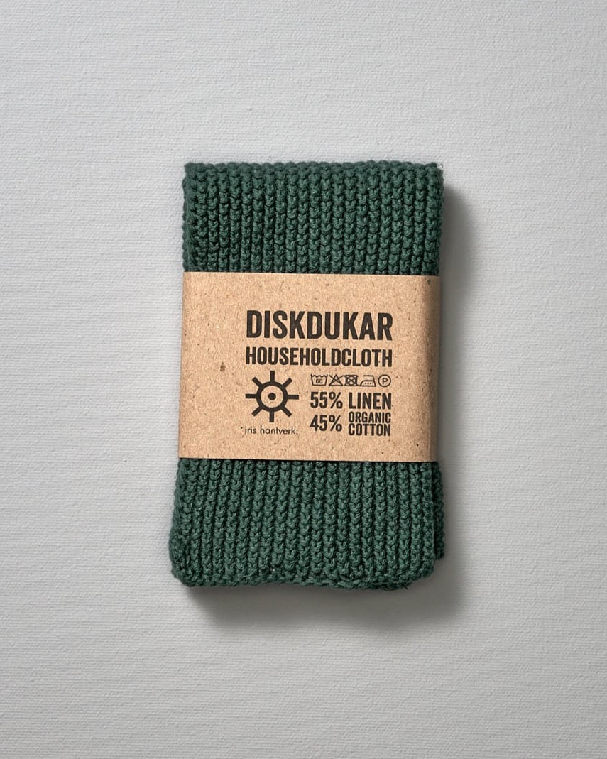 An Iris Hantverk Linen Household Cloth in Pine Green on a grey surface, made of an absorbent linen/cotton blend fabric.