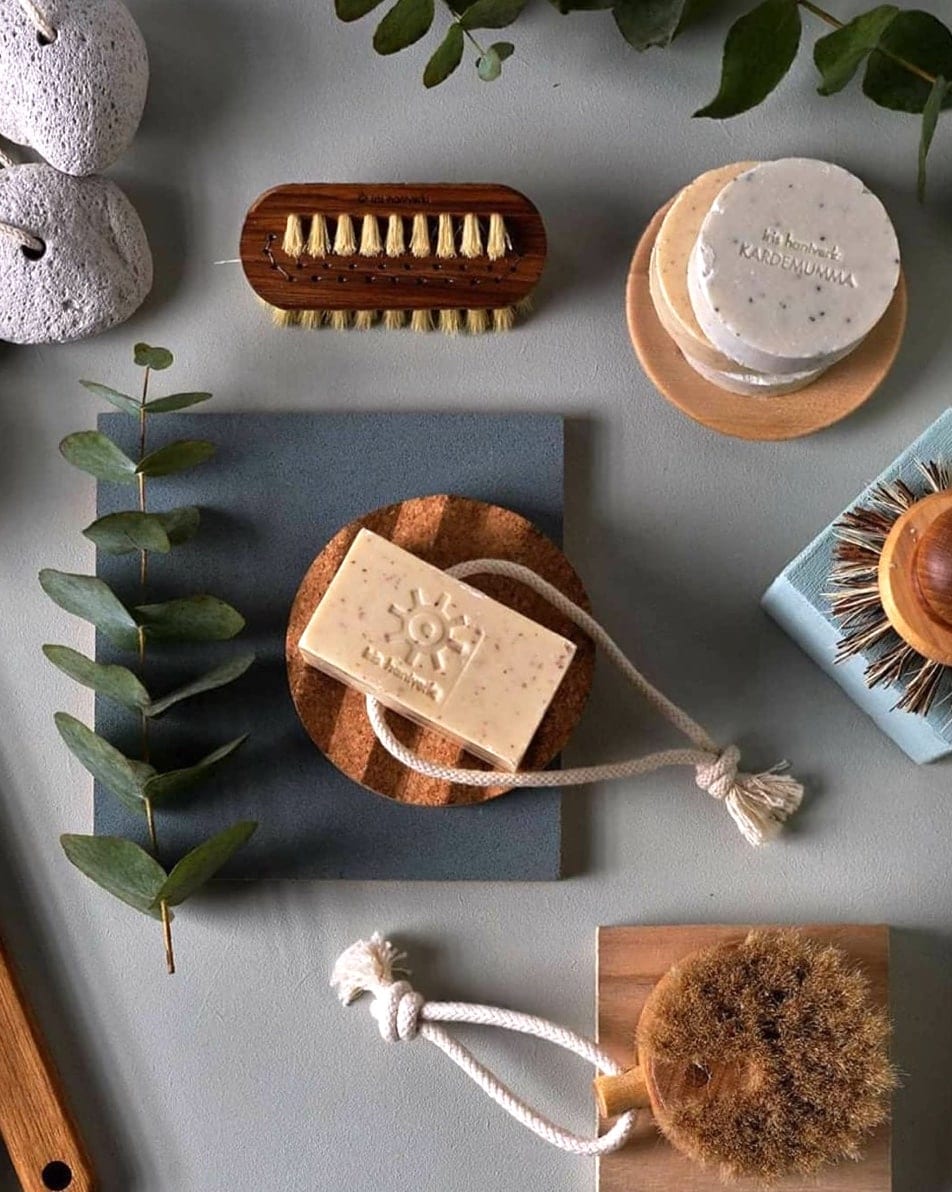 A variety of Iris Hantverk Cork Soap Dishes, scrubs, and other items are laid out on a table.