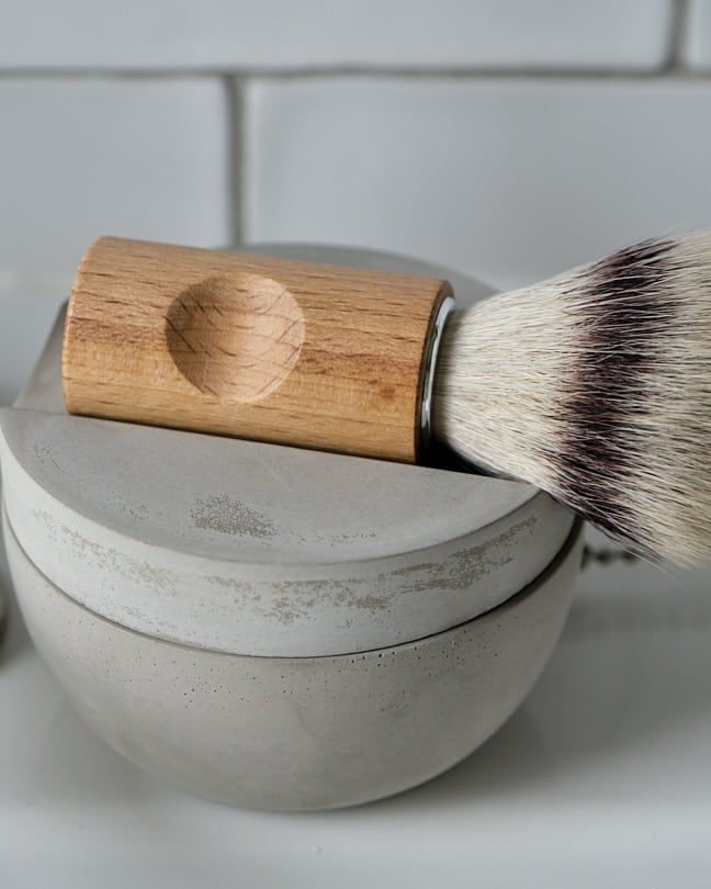 The Iris Hantverk Shaving Brush & Cup Set with Cedarwood Soap – Bundle is shown, featuring a wooden-handled brush atop a round cedarwood soap container, set against a plain gray background.
