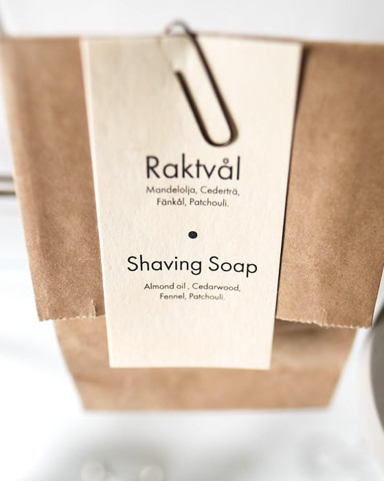 A bar of Iris Hantverk Shaving Soap – Cedarwood next to a brown paper bag.