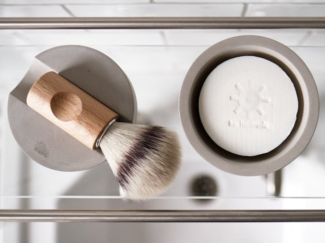 A Iris Hantverk shaving brush - Silver Tip and soap on a shelf in a bathroom.