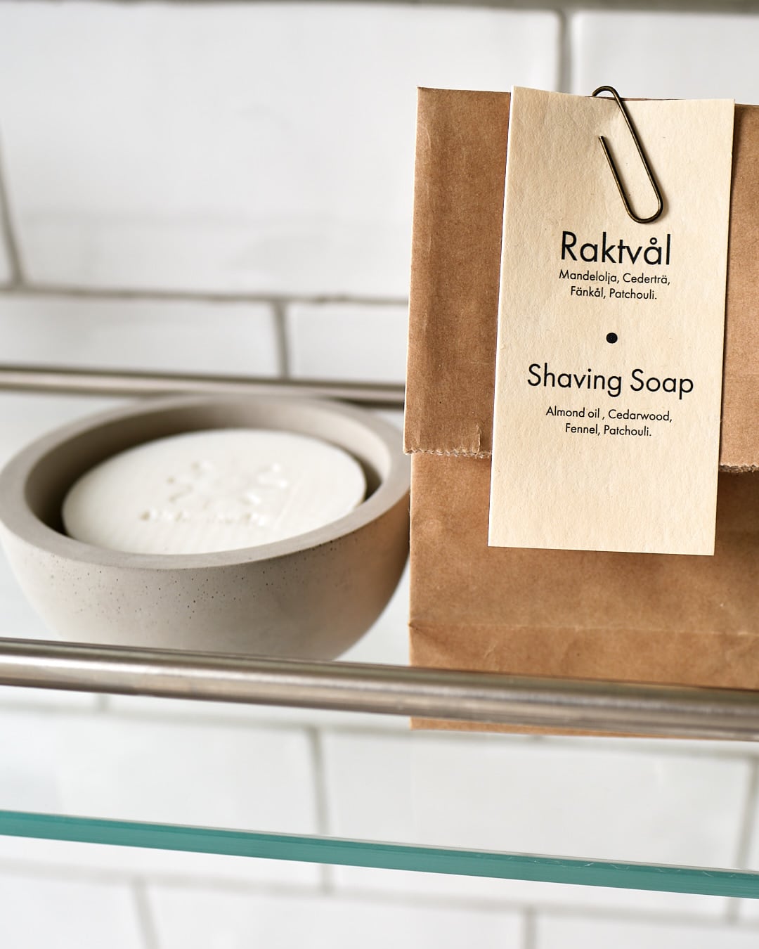 The Iris Hantverk Shaving Brush & Cup Set with Cedarwood Soap – Bundle rests on a glass shelf, with the cedarwood soap and classic shaving brush displayed against white tiles.