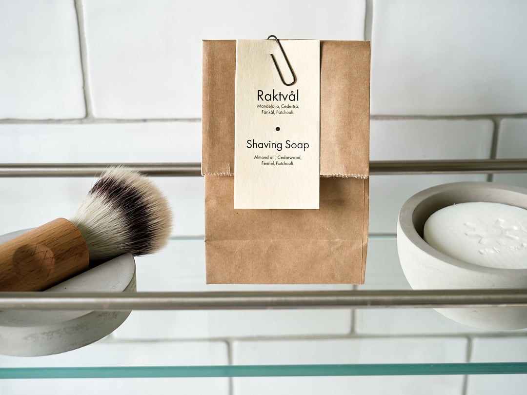 A paper bag with a Shaving Cup with Cedarwood Shaving Soap from Iris Hantverk on a shelf.