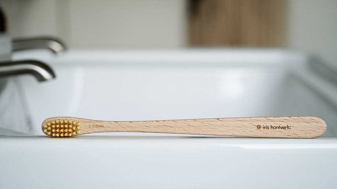 An Iris Hantverk wooden toothbrush sits on top of a sink.