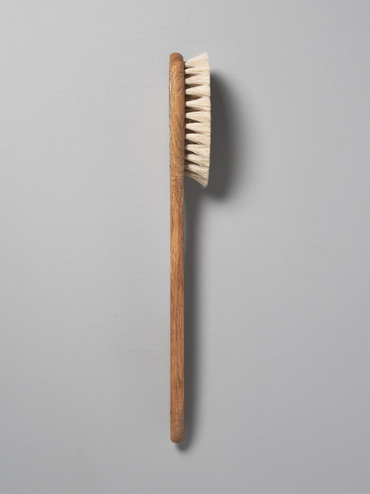 An Iris Hantverk Body Brush – Oval Head with a wooden handle on a gray background.