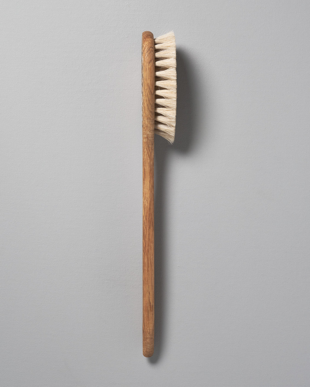 An Iris Hantverk Body Brush – Oval Head with a wooden handle on a gray background.
