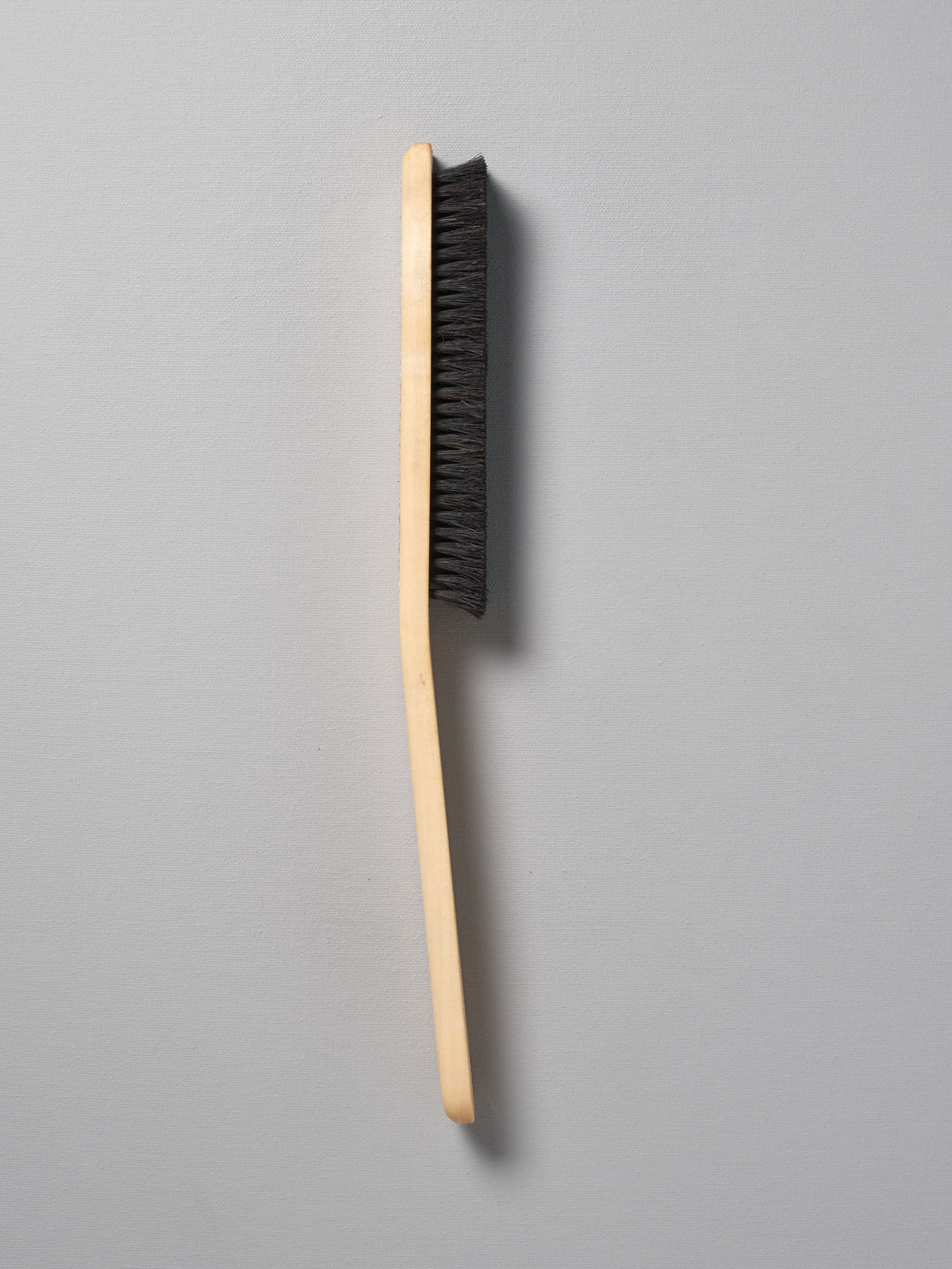 An Iris Hantverk Clothes Brush with black bristles on a gray background.