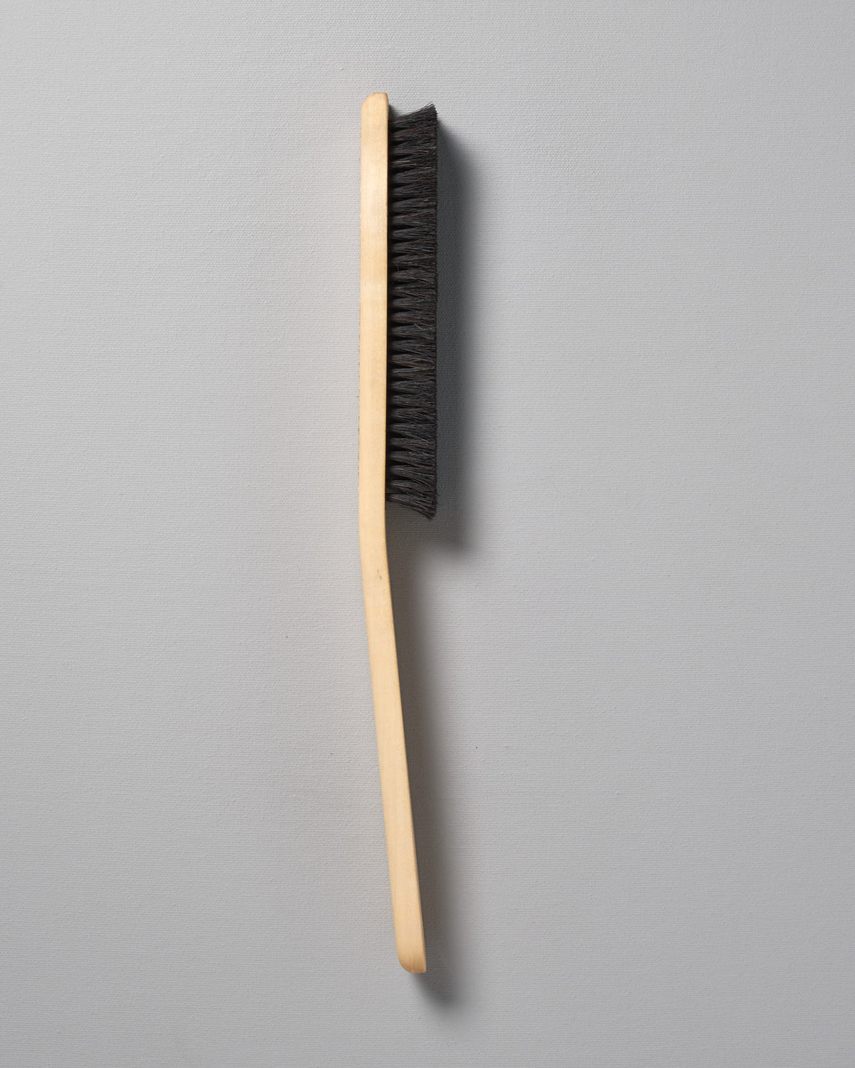 An Iris Hantverk Clothes Brush with black bristles on a gray background.