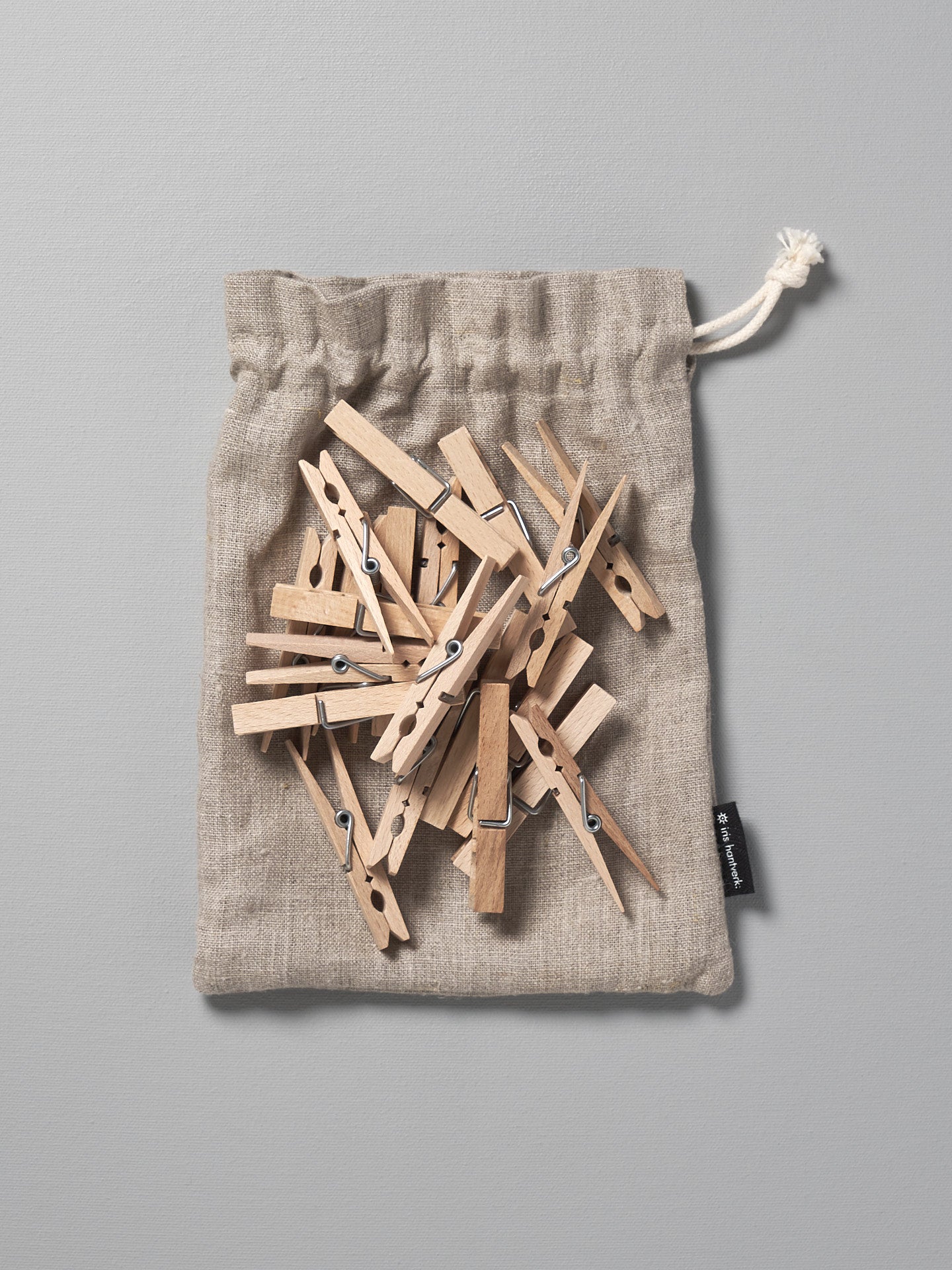 A collection of Iris Hantverk Clothes Pegs – 20pcs inside a drawstring bag lying on a gray surface.
