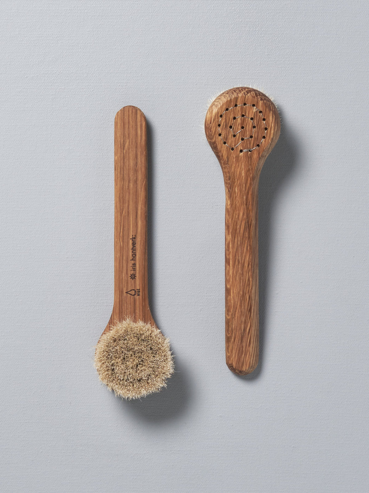 Two Iris Hantverk Face Brushes - Wet next to each other on a white surface.