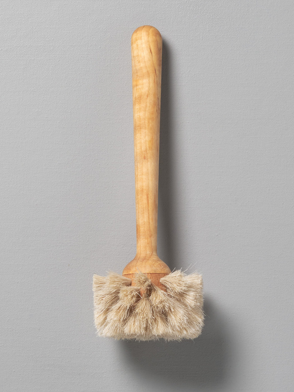 An Iris Hantverk glass brush with a wooden handle on a gray background.