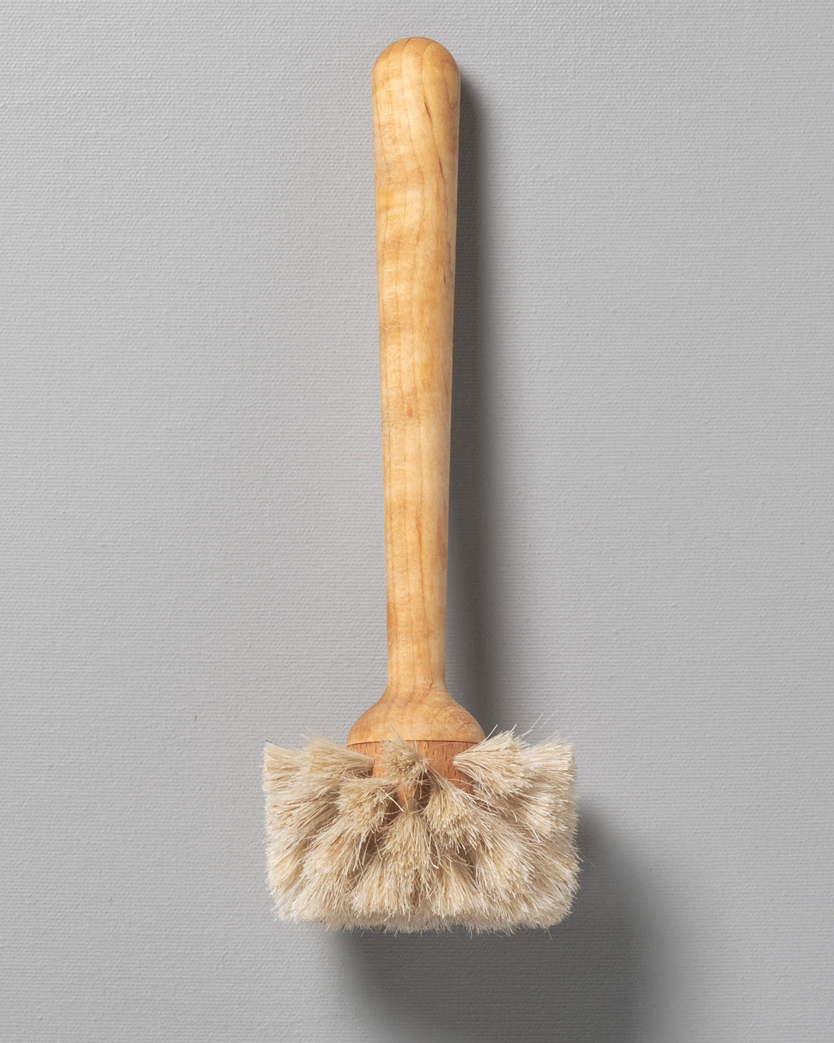 An Iris Hantverk glass brush with a wooden handle on a gray background.