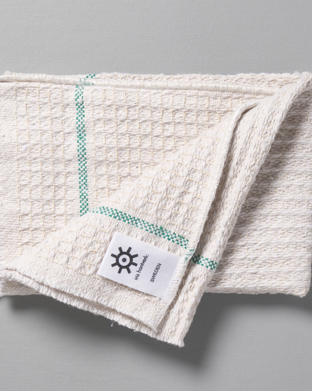 An Iris Hantverk white towel with a green stripe on it.