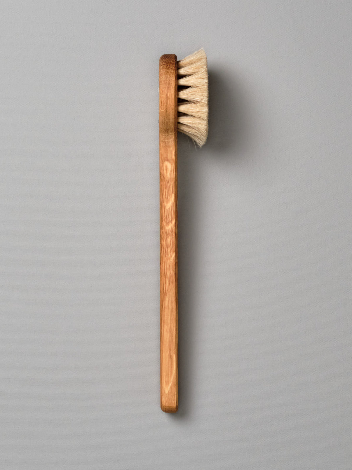 An Iris Hantverk Body Brush - Round Head with a handle on a gray background.