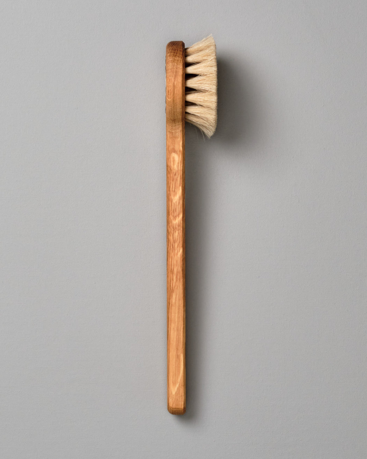 An Iris Hantverk Body Brush - Round Head with a handle on a gray background.