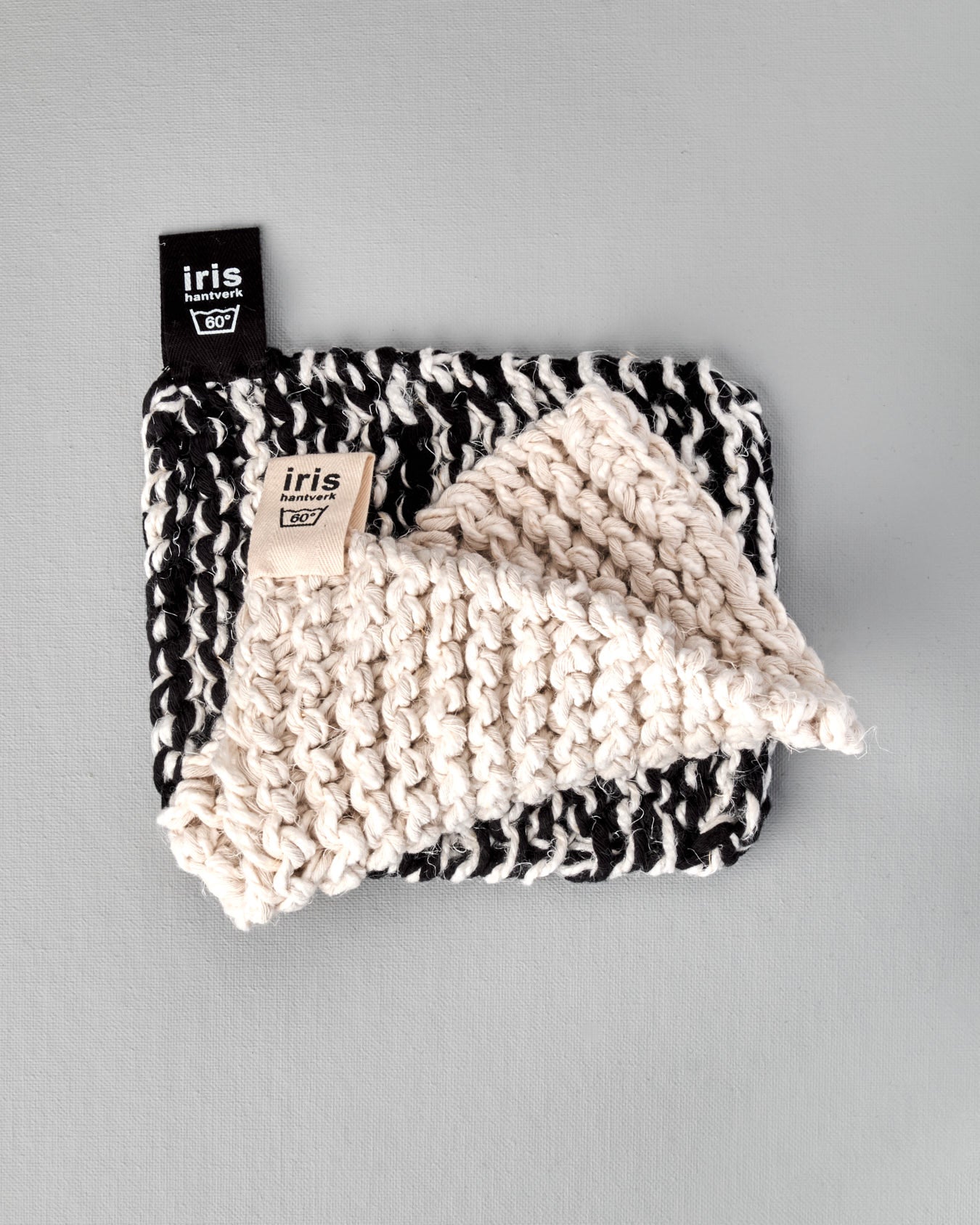 A black and white Iris Hantverk knitted Pot & Oven-tray Holder with a tag on it.