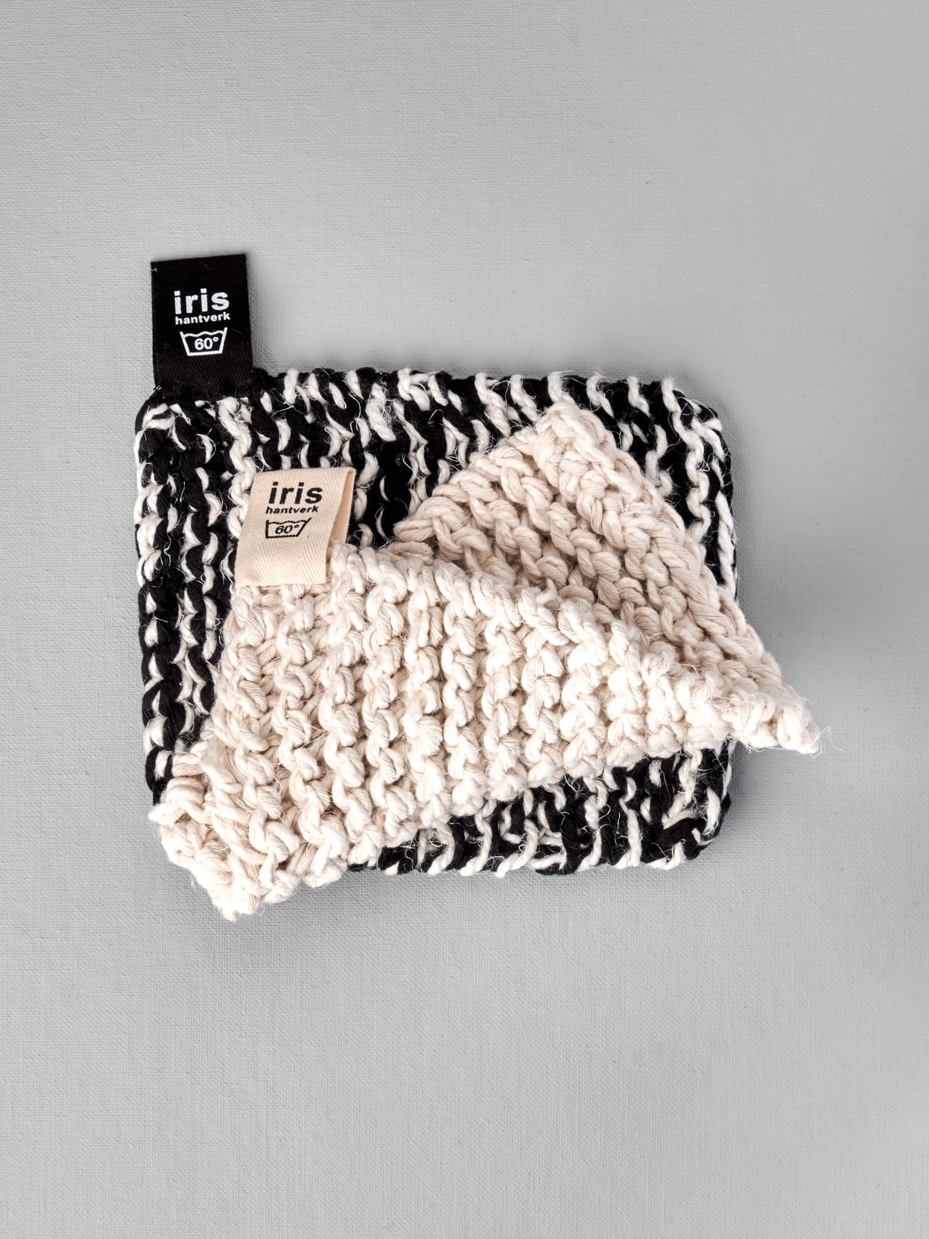 A black and white Iris Hantverk knitted Pot & Oven-tray Holder with a tag on it.