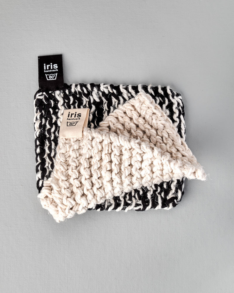 A black and white Iris Hantverk knitted Pot & Oven-tray Holder with a tag on it.