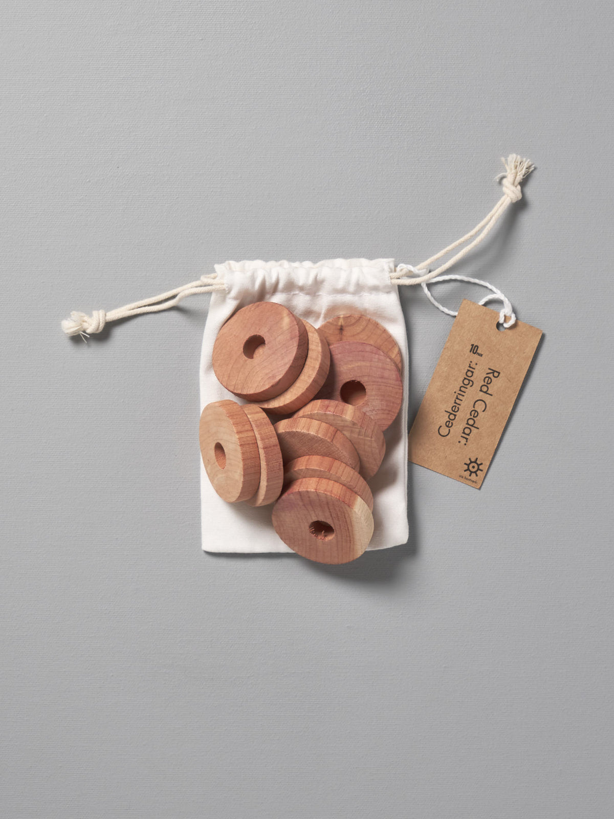 Red Cedar Rings – 10pcs by Iris Hantverk in a bag on a grey background.