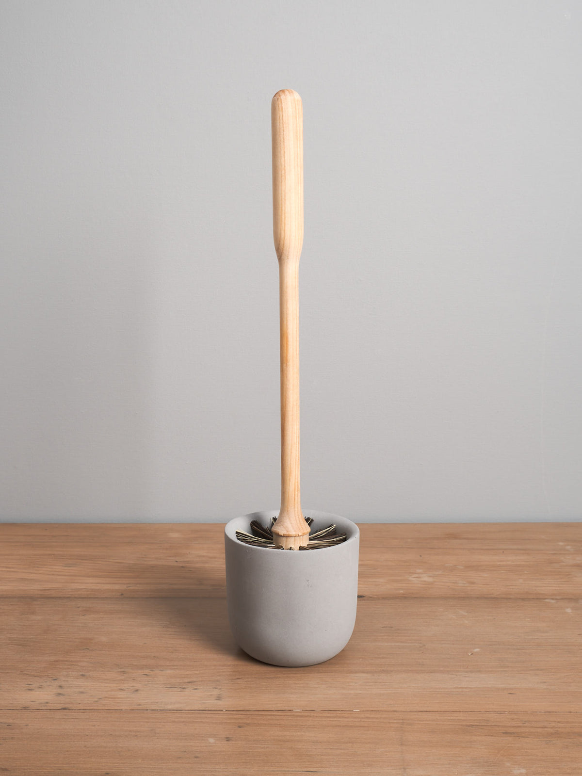 An Iris Hantverk toilet brush with a concrete cup on top of a wooden table.