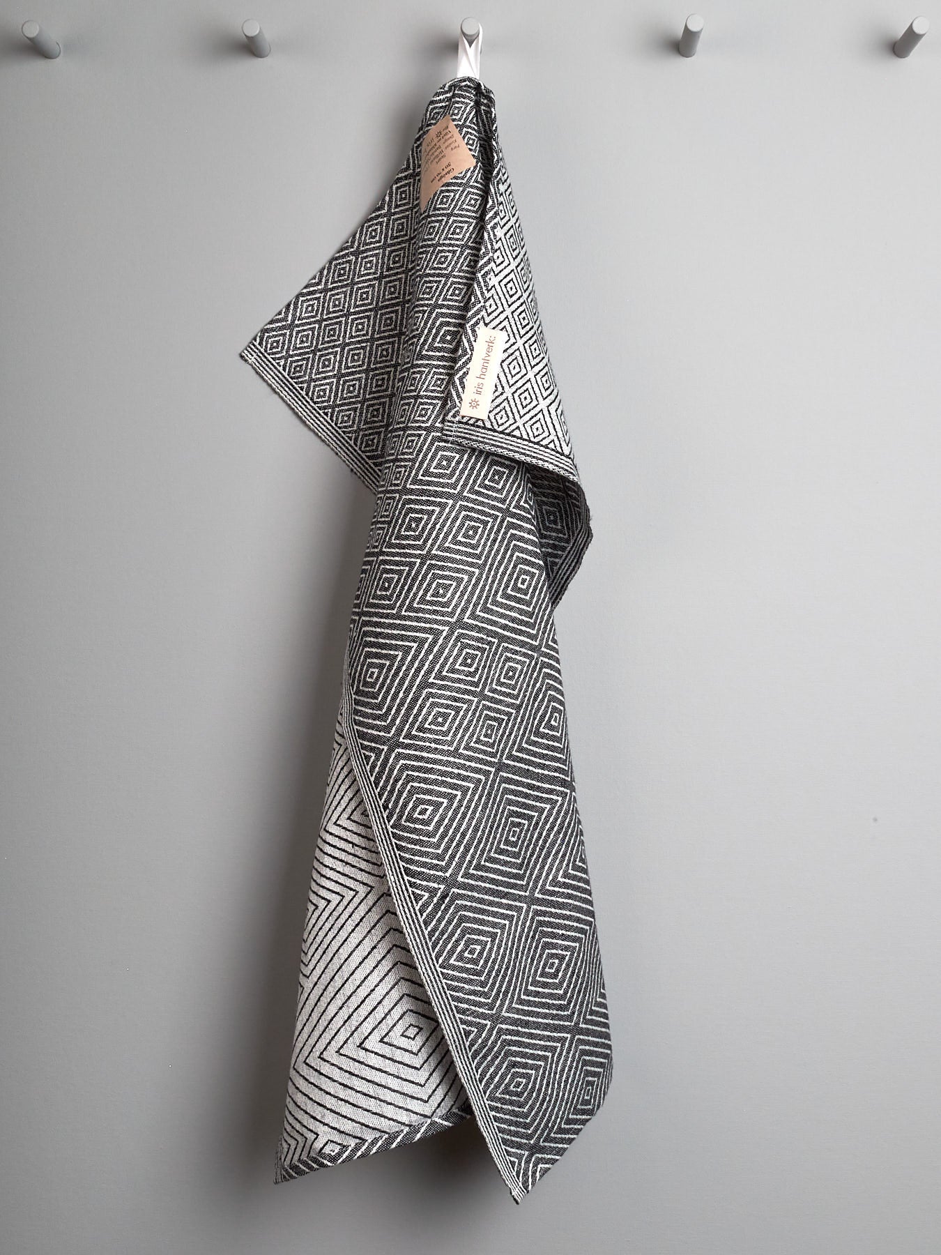 An Iris Hantverk black and white tea towel hanging on a hook.