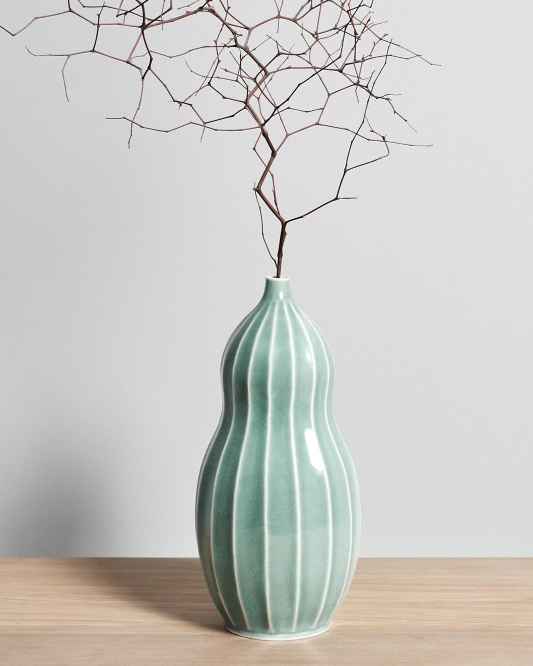 A Gourd Vase - Celadon by Jino Ceramic Studio with a twig in it.