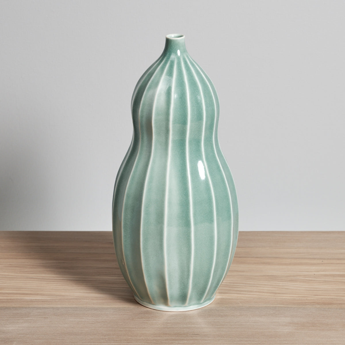 A Gourd Vase - Celadon sitting on a wooden table manufactured by Jino Ceramic Studio.