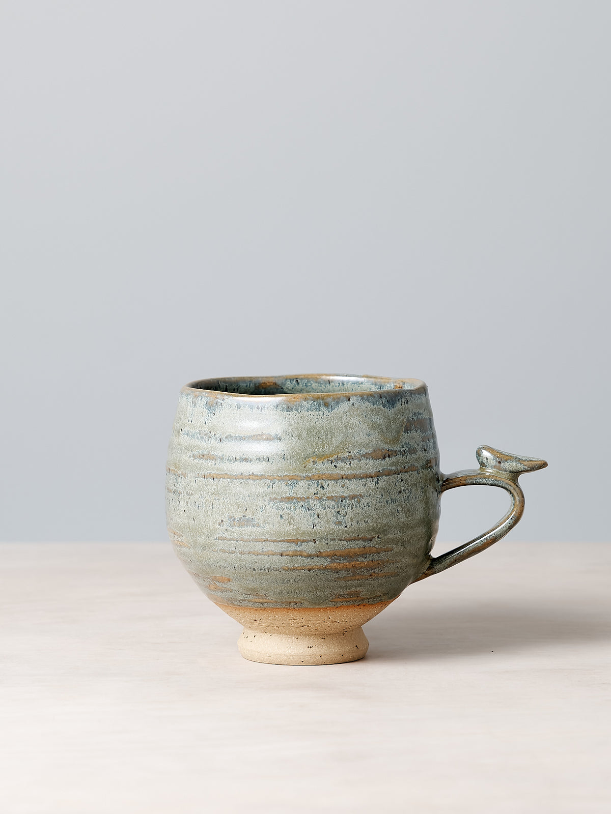 A small Bird Handle Cup – Green Tea from Jino Ceramic Studio, with a bird on it, sitting on a table.