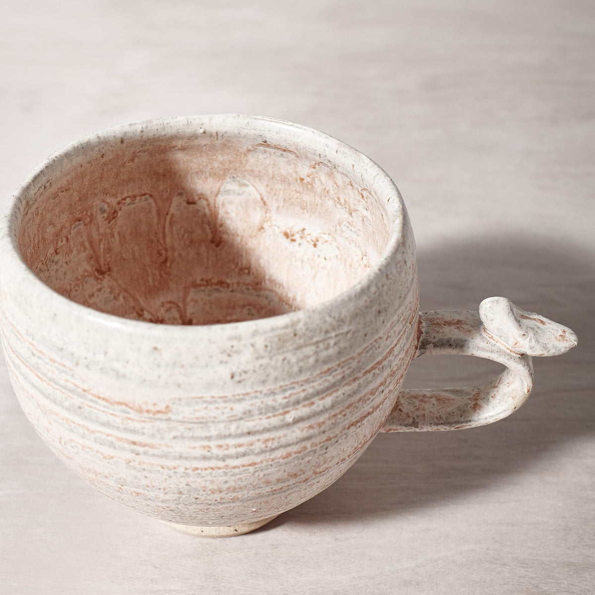 A Bird Handle Cup – Pink Salt with a handle on a wooden table. Brand Name: Jino Ceramic Studio
