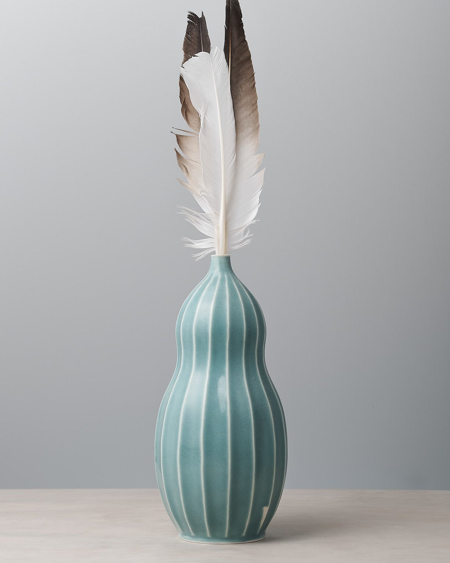 A Gourd Vase - Celadon from Jino Ceramic Studio with a feather in it.