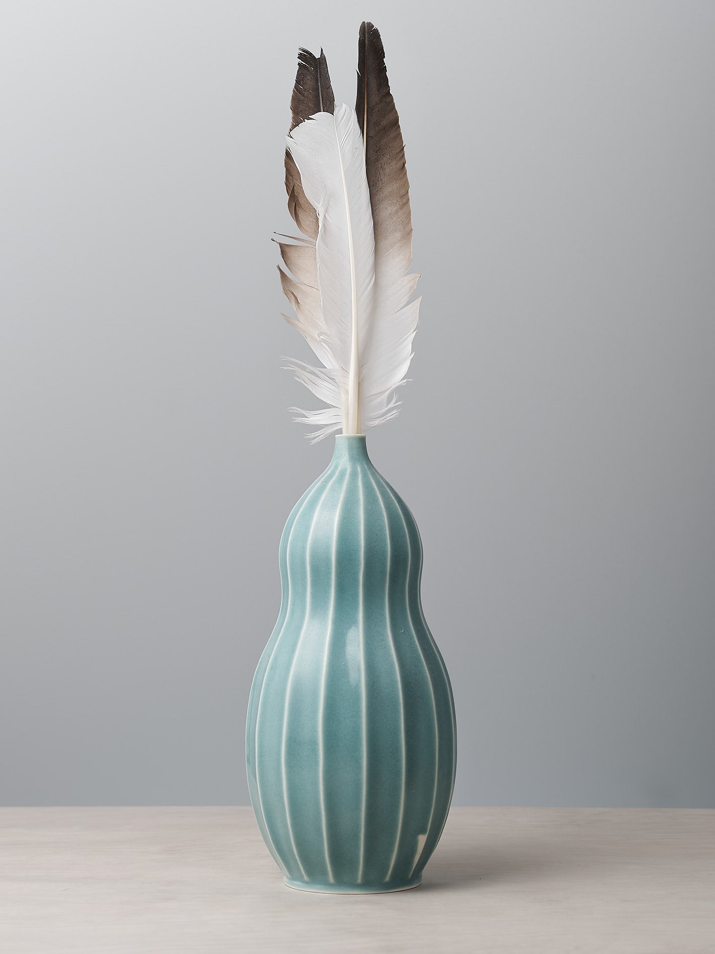 A Gourd Vase - Celadon from Jino Ceramic Studio with a feather in it.