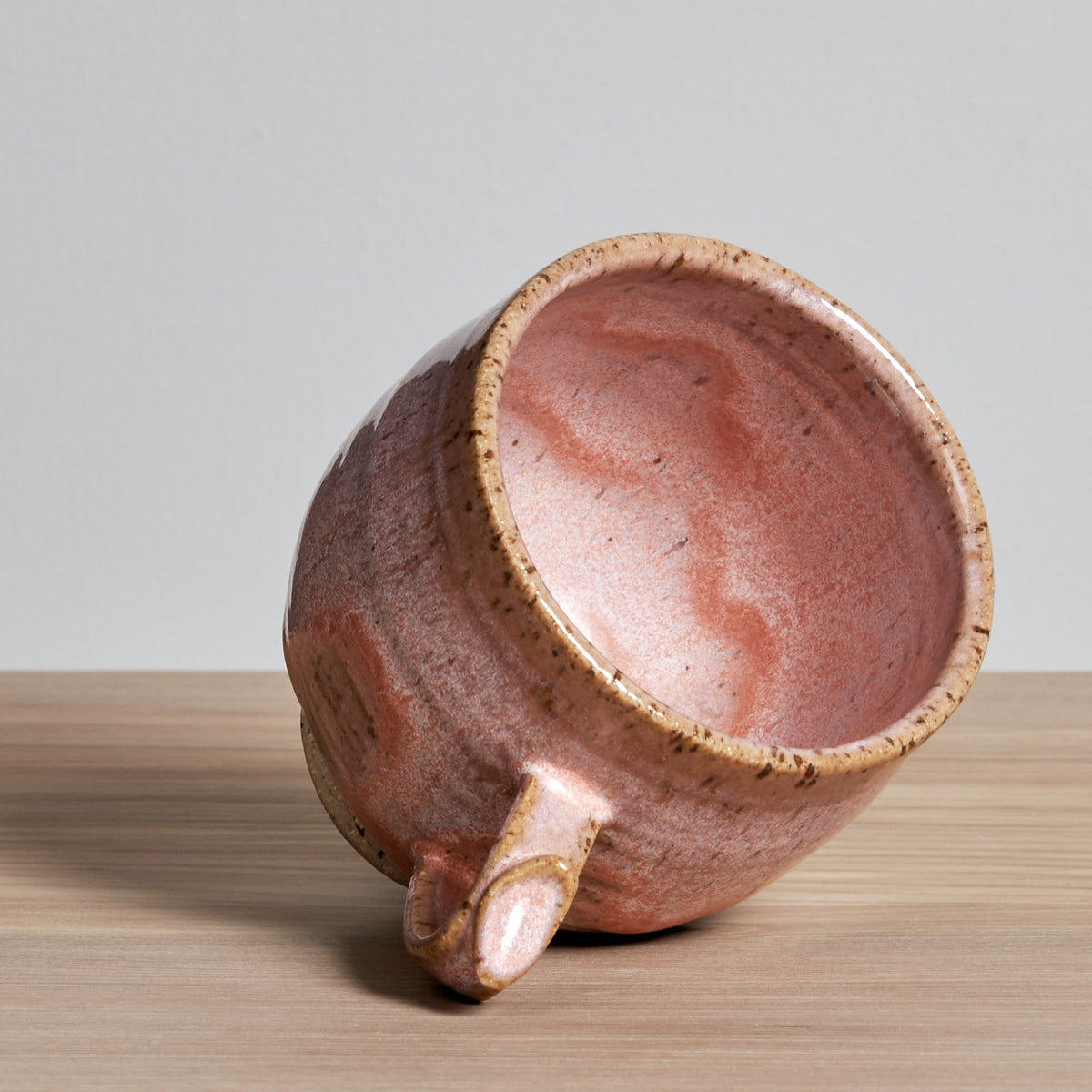 A Bird Handle Cup - Rhubarb from Jino Ceramic Studio sitting on a wooden table.