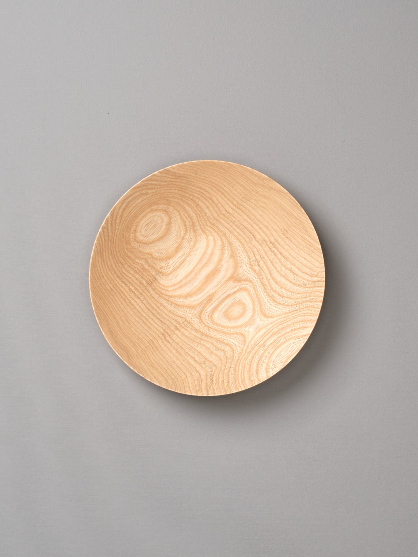 A round Kihachi wooden plate on a gray background.