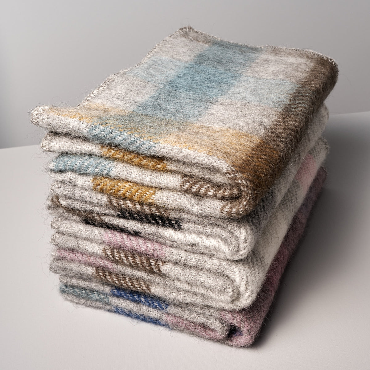 A stack of Gotland Wool Baby Throws - Multi Pink by Klippan on a white surface.