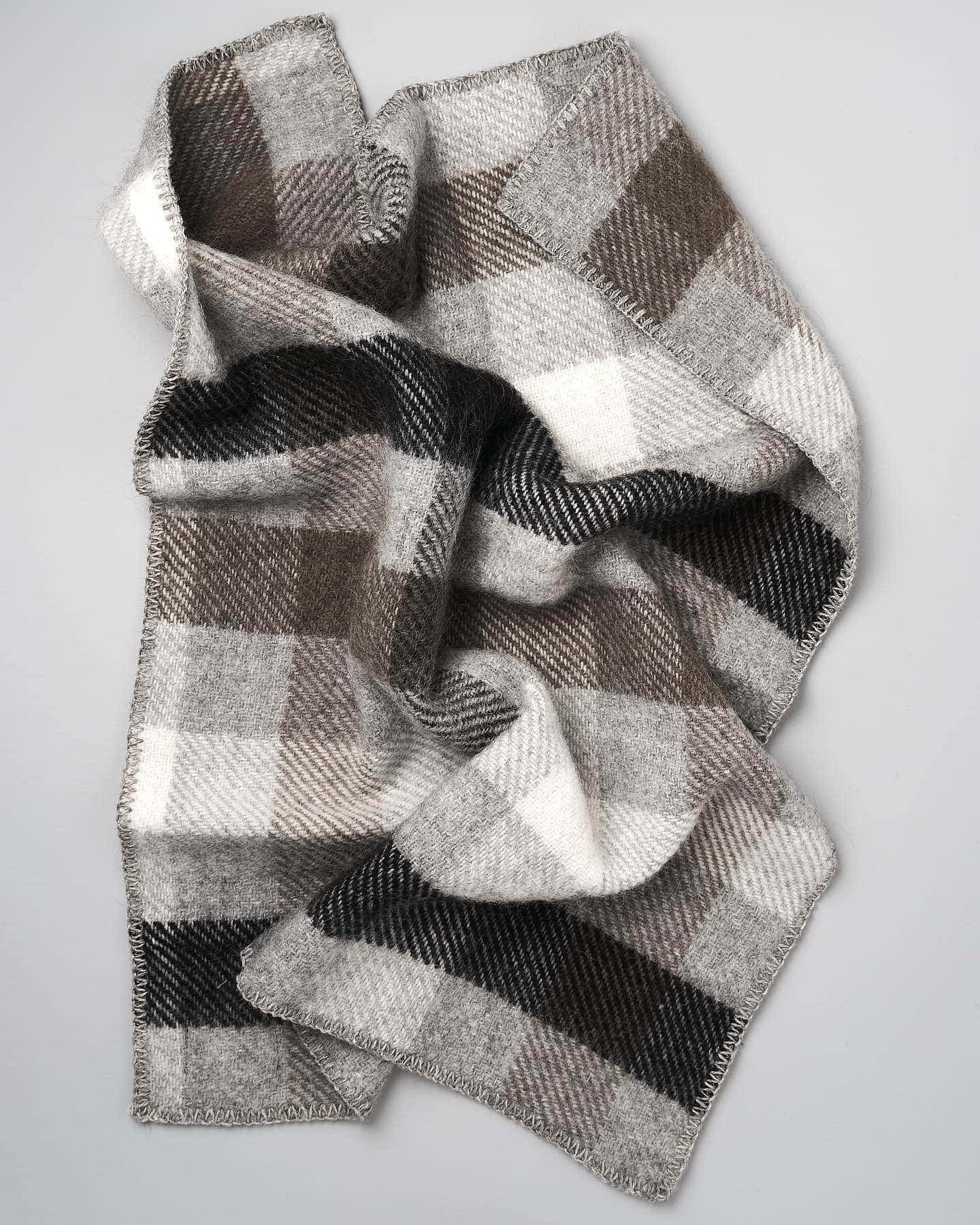 A Gotland Wool Baby Throw – Multi Grey, featuring a classic brown, gray, and beige plaid pattern inspired by timeless Klippan of Sweden designs, is displayed on a plain gray surface.